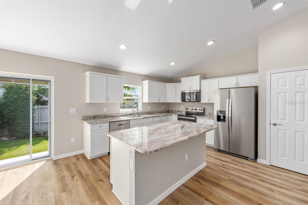 A kitchen with white cabinets, a stone island, stainless steel appliances, and wood-look flooring — 10910 N TARTAN TERRACE, CITRUS SPRINGS, FL