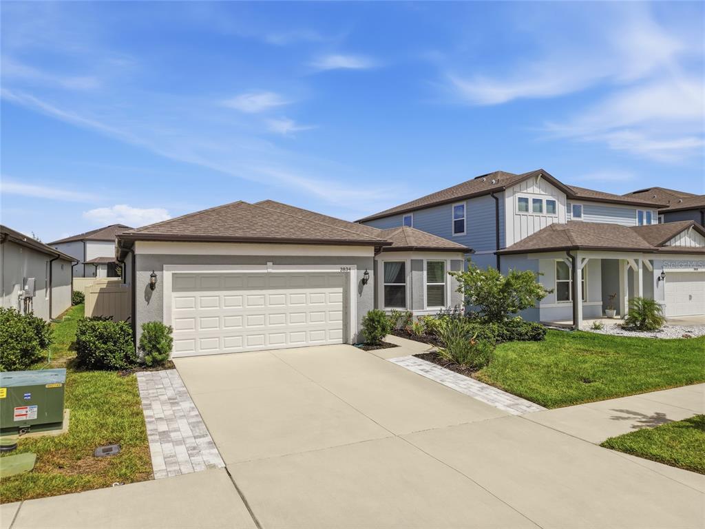 A single-story house with a two-car garage and a paved driveway under a blue sky — 3834 MAPLE BAY LANE, LAND O LAKES, FL