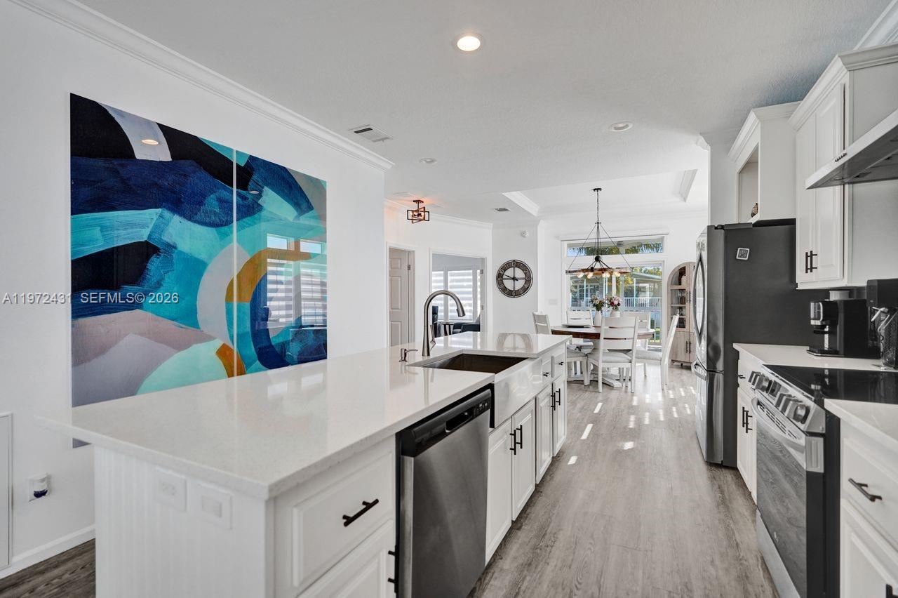 A modern white kitchen features a large island, stainless steel appliances, and abstract wall art — 4035 Marigold Rd, Boynton Beach FL 33436, BOYNTON BEACH, FL