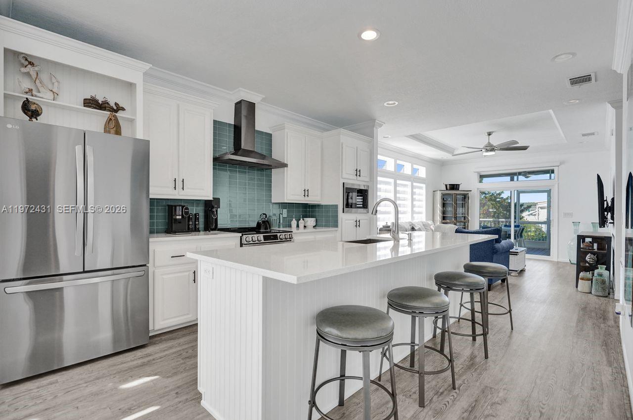 A modern kitchen features white cabinetry, a teal tile backsplash, and a large center island — 4035 Marigold Rd, Boynton Beach FL 33436, BOYNTON BEACH, FL