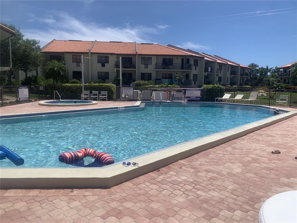 A wooden deck features picnic tables and a grill overlooking a fenced swimming pool area — 1515 PINELLAS BAYWAY S UNIT 34, ST PETERSBURG, FL