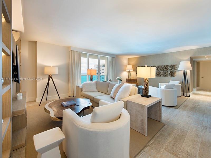 A modern living room features a sectional sofa, white armchairs, and ocean views through windows — 102 24th St # 1540, Miami Beach FL 33139, MIAMI BEACH, FL