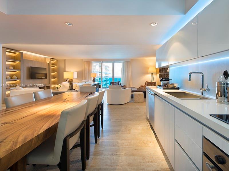 A modern kitchen with white cabinets and a large wooden dining table in an open-concept room — 102 24th St # 1540, Miami Beach FL 33139, MIAMI BEACH, FL