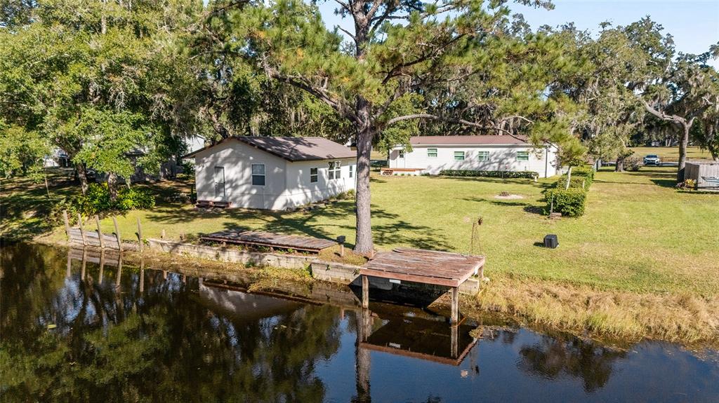 A wooden dock sits on the edge of a canal surrounded by trees and grass — 2008 N RETREAT, INVERNESS, FL