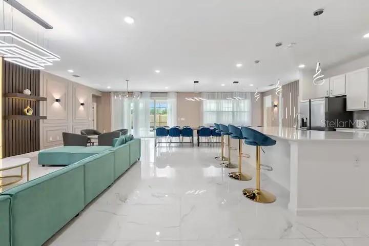 An open-concept living room and kitchen featuring a large teal sectional and white marble floors — 3870 SONOMA BLVD, KISSIMMEE, FL
