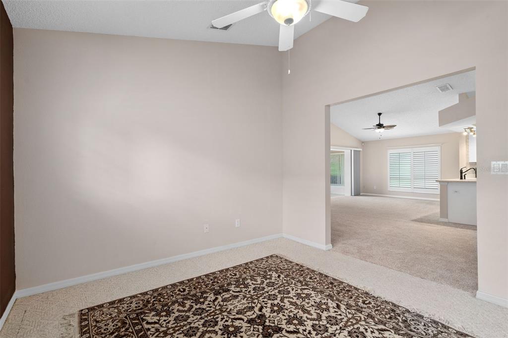 A carpeted room with a ceiling fan opens into a living area with a kitchen — 3525 ROLLINGBROOK STREET, CLERMONT, FL