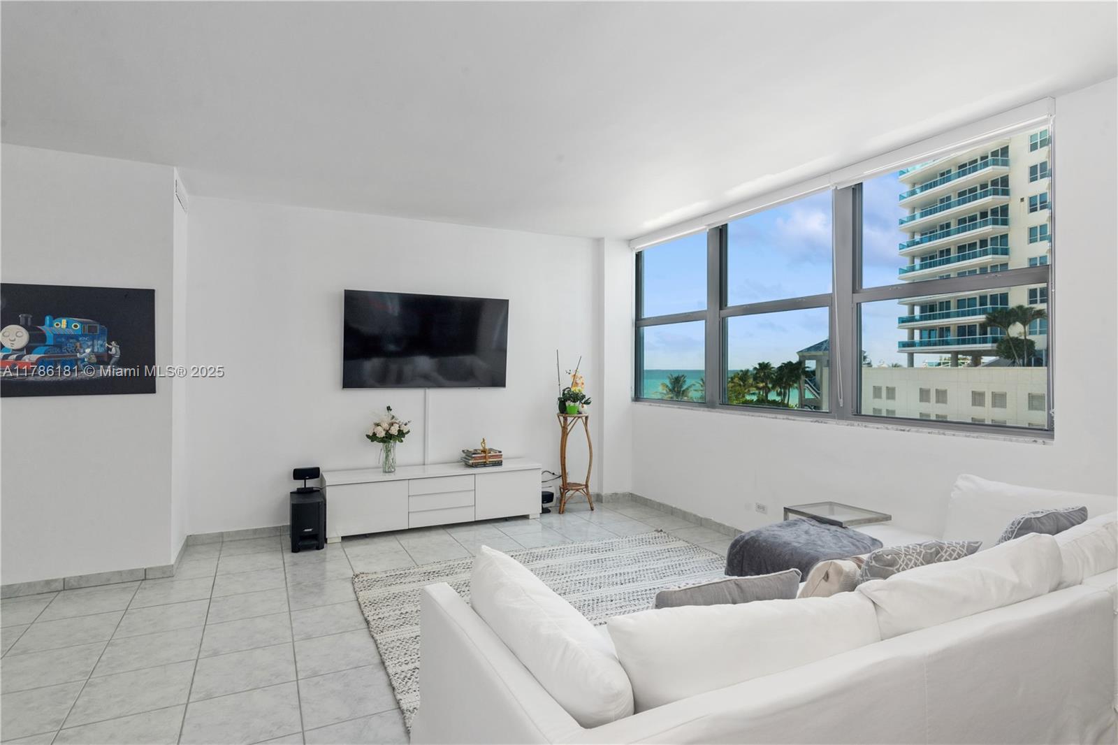 A bright living room features white walls, tile flooring, a wall-mounted television, and ocean views — 5055 Collins Ave # 5F, Miami Beach FL 33140, MIAMI BEACH, FL