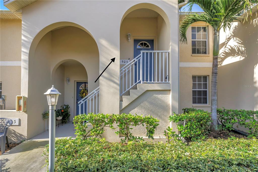 The exterior of a two-story stucco building features arched entryways, blue doors, and stairs — 8350 WINGATE DRIVE UNIT 925, SARASOTA, FL