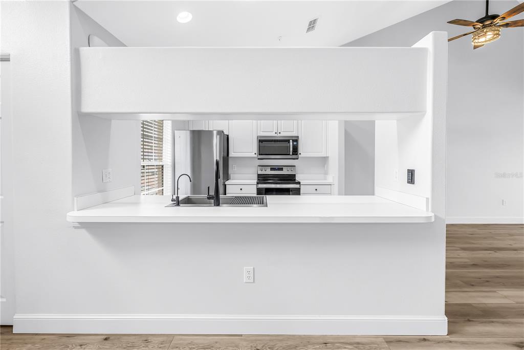 A kitchen features a white pass-through counter, stainless steel appliances, and light wood flooring — 8350 WINGATE DRIVE UNIT 925, SARASOTA, FL