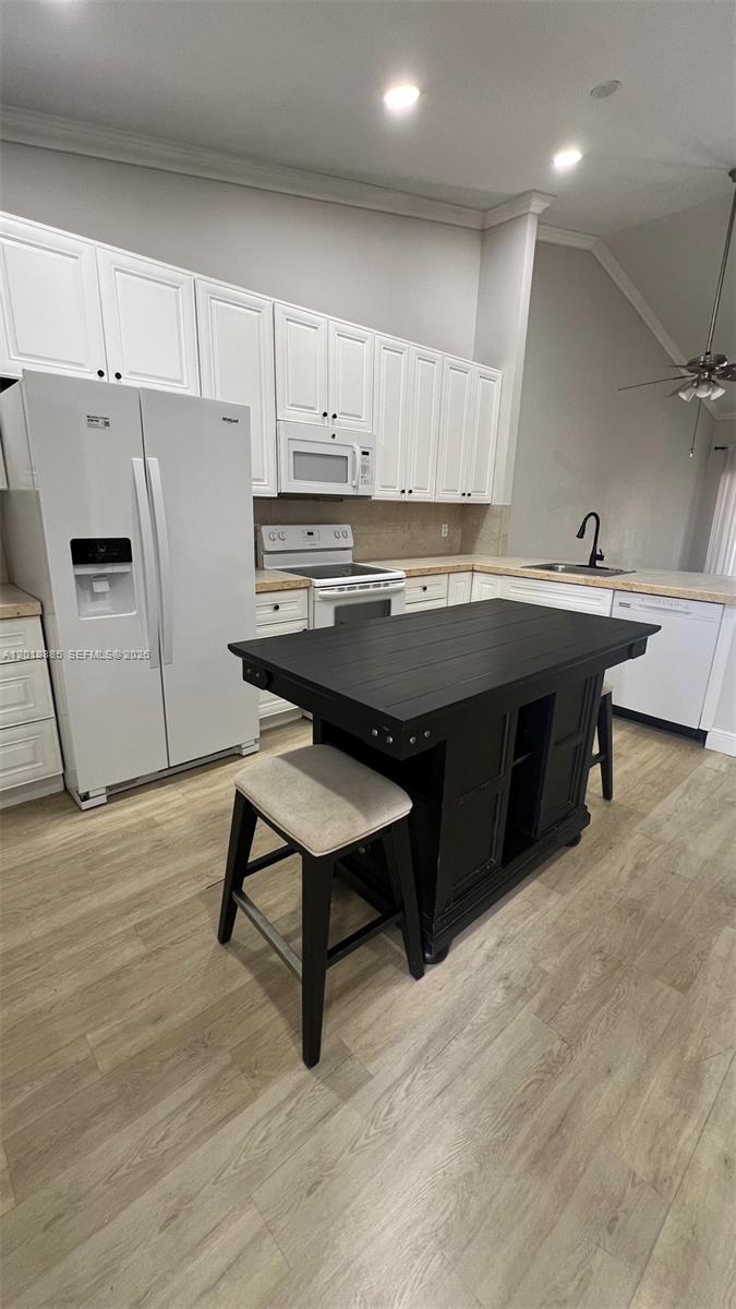 A kitchen features white cabinets, stainless steel appliances, light wood flooring, and a black island — 11065 NW 38th Pl, Sunrise FL 33351, SUNRISE, FL