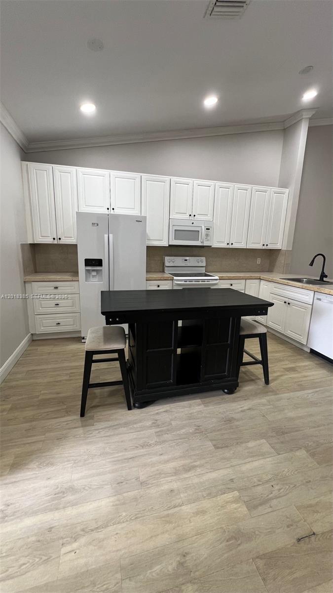A kitchen features white cabinets, a black island with two stools, and light wood flooring — 11065 NW 38th Pl, Sunrise FL 33351, SUNRISE, FL