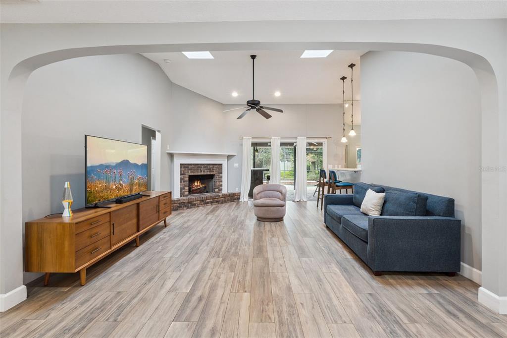 A living room with wood-look flooring, a brick fireplace, a blue sofa, and vaulted ceilings — 4507 WINDERWOOD CIRCLE, ORLANDO, FL
