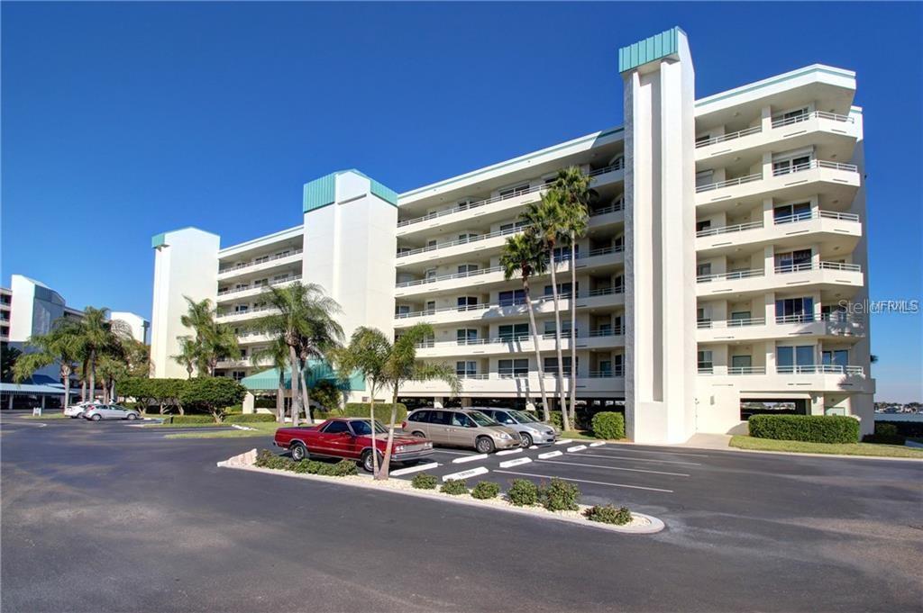 A multi-story white apartment building with balconies stands behind a paved parking lot — 7979 SAILBOAT KEY BOULEVARD S UNIT 306, SOUTH PASADENA, FL