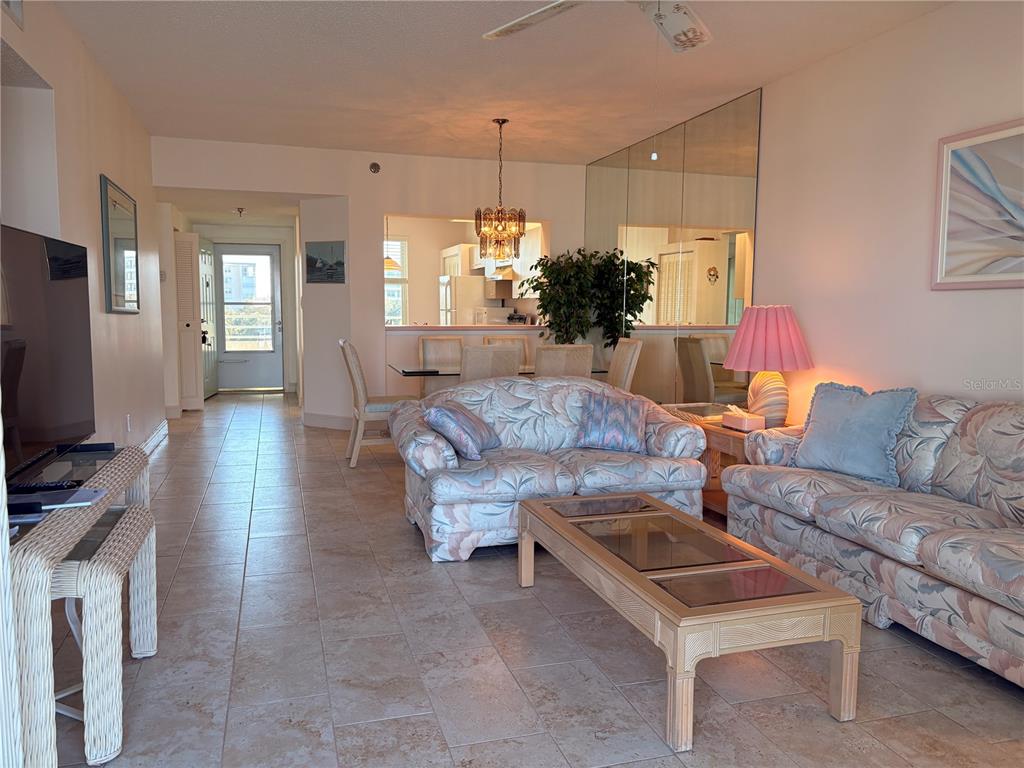 A living room with tile floors, floral sofas, a coffee table, and an adjacent dining area — 7979 SAILBOAT KEY BOULEVARD S UNIT 306, SOUTH PASADENA, FL
