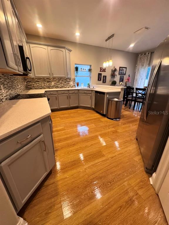 A kitchen features light gray cabinets, stainless steel appliances, and polished wood-look flooring — 6956 BRESCIA WAY, ORLANDO, FL