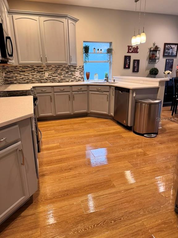A kitchen features gray cabinets, light countertops, a tiled backsplash, and glossy wood-look flooring — 6956 BRESCIA WAY, ORLANDO, FL