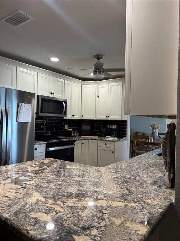 A kitchen features white cabinets, granite countertops, a black tile backsplash, and stainless steel appliances — 17071 WATERS EDGE CIRCLE, NORTH FORT MYERS, FL