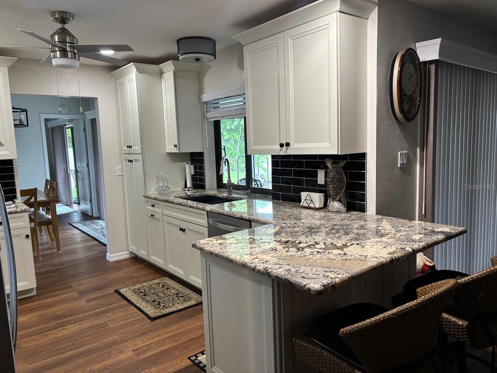 A kitchen features white cabinets, granite countertops, a black tile backsplash, and wood-look flooring — 17071 WATERS EDGE CIRCLE, NORTH FORT MYERS, FL