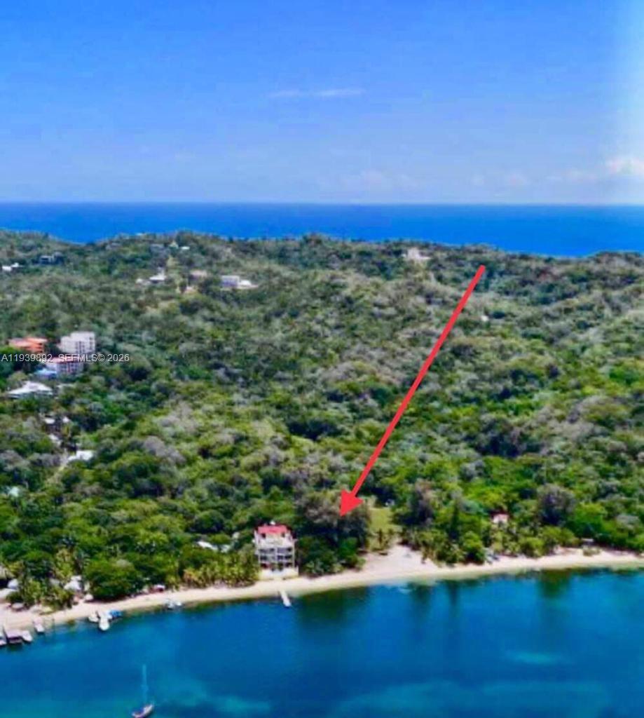 An aerial view shows a multi-story building situated on a beach surrounded by dense forest — Roatan Island at Caribbean, Honduras, NA, NA
