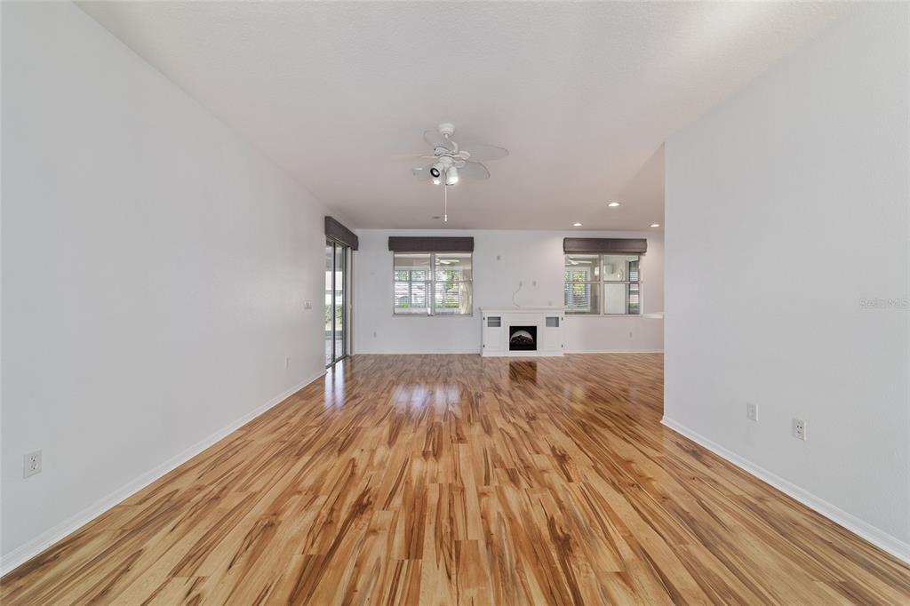 A spacious living room features light-colored walls, wood-look flooring, a ceiling fan, and a fireplace — 8798 SW 83RD CIRCLE, OCALA, FL