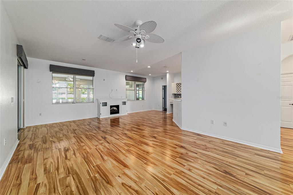 An open-concept living room features wood-look flooring, a ceiling fan, and a white fireplace — 8798 SW 83RD CIRCLE, OCALA, FL