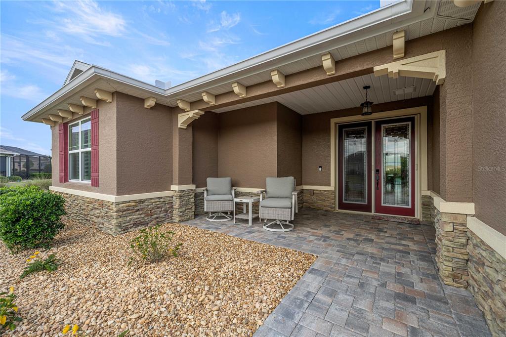 A covered front porch features stone veneer, a paver floor, and two outdoor chairs — 8477 SW 93RD CIRCLE, OCALA, FL