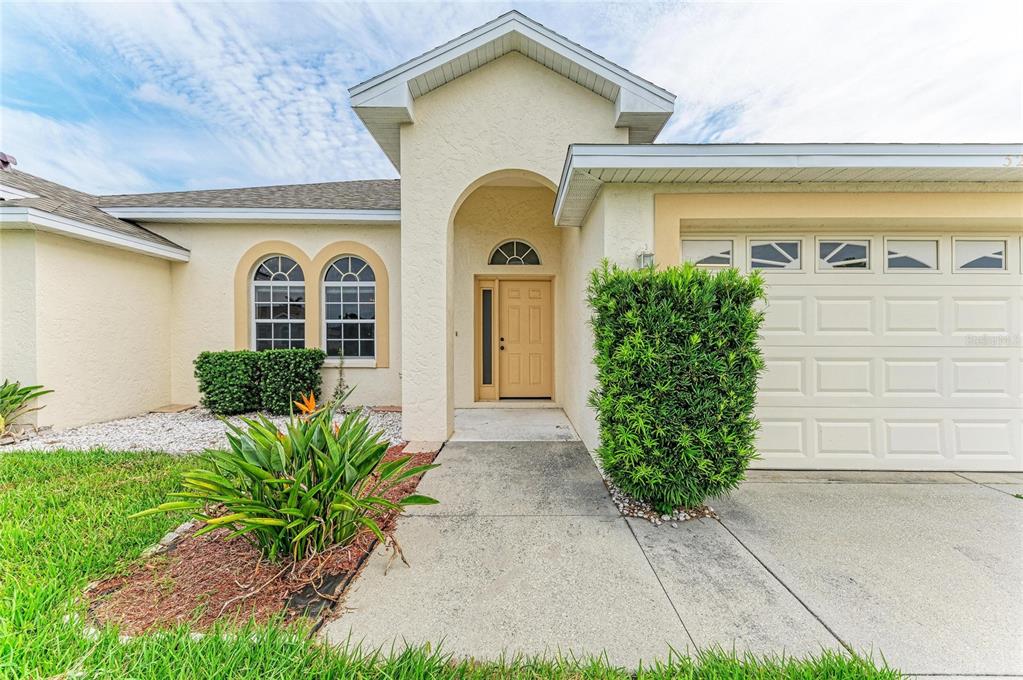 A beige single-story house exterior features a covered entryway, a two-car garage, and arched windows — 3213 45TH AVENUE E, BRADENTON, FL