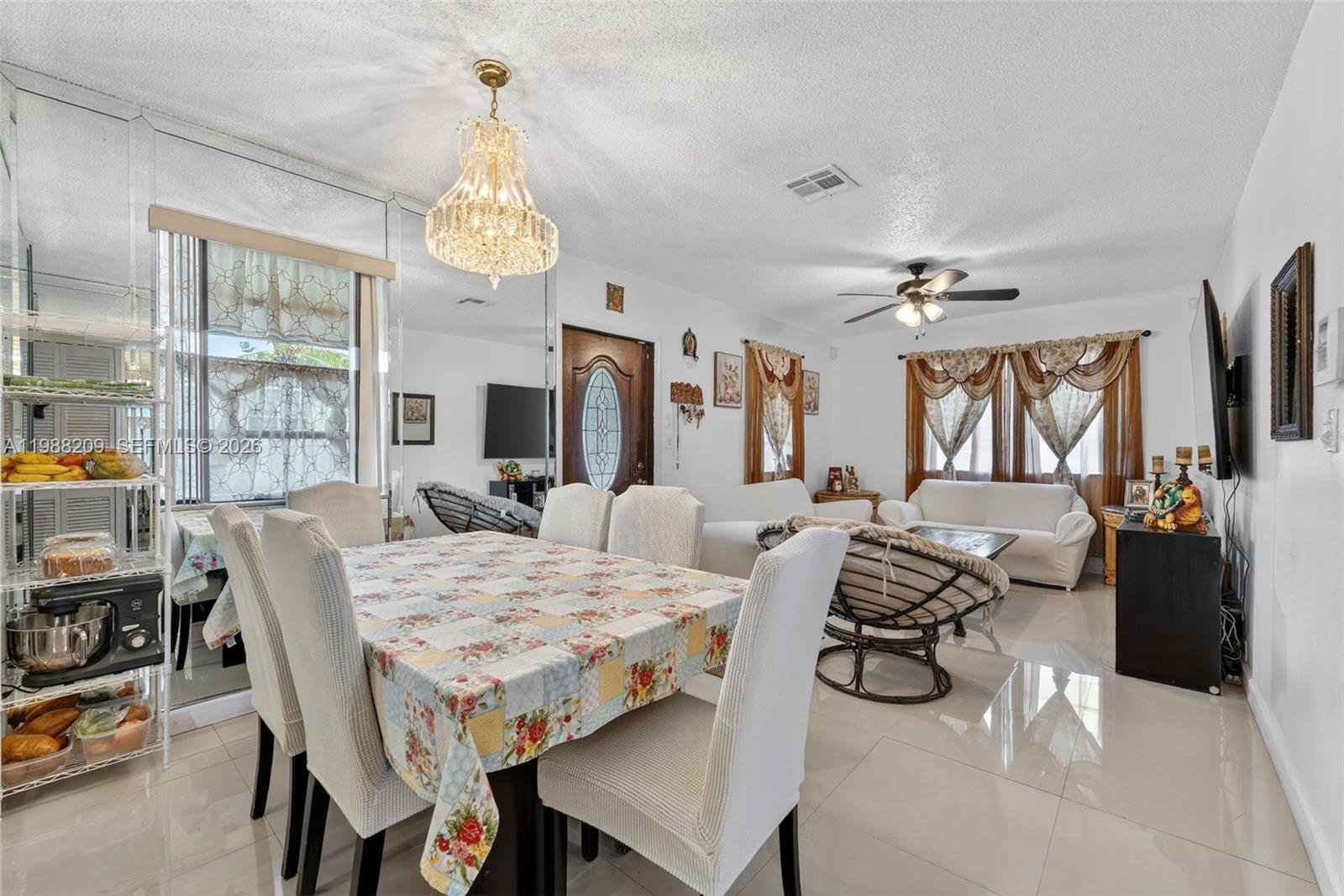 A dining area with a floral tablecloth and chandelier opens into a living room — 26672 SW 137th Ct, Miami FL 33032, MIAMI, FL