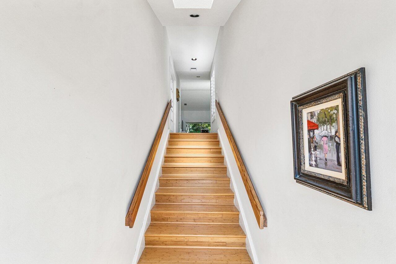 A staircase with wooden steps and handrails leads to a hallway with a framed painting — 17061 Emile Street # 5, Boca Raton FL 33487, BOCA RATON, FL