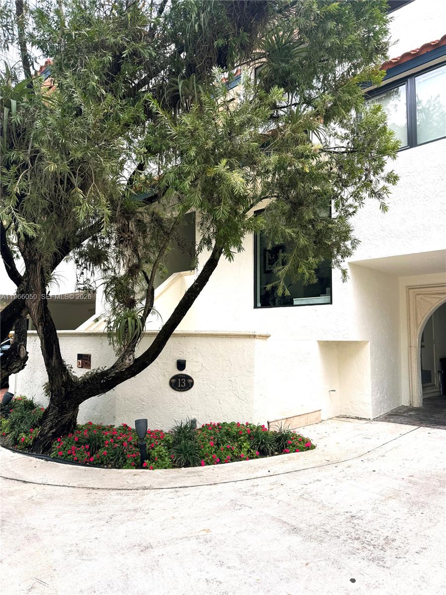 A white stucco building exterior features a large tree and a small garden bed — 2000 S Bayshore Drive # 13, Miami FL 33133, MIAMI, FL