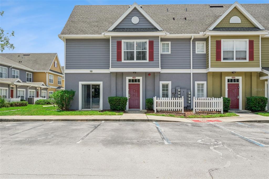 A two-story townhouse with gray and olive siding, red doors, and a parking lot — 2611 GALA ROAD N UNIT 108, KISSIMMEE, FL