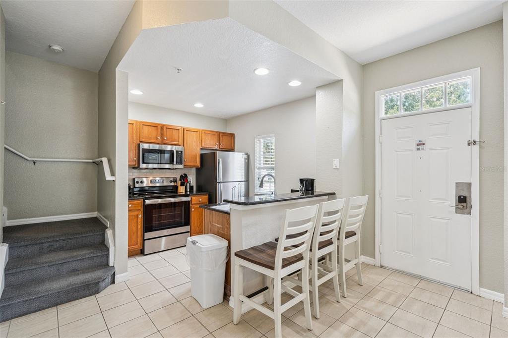 A kitchen with wood cabinets, stainless steel appliances, and a breakfast bar next to stairs — 2611 GALA ROAD N UNIT 108, KISSIMMEE, FL