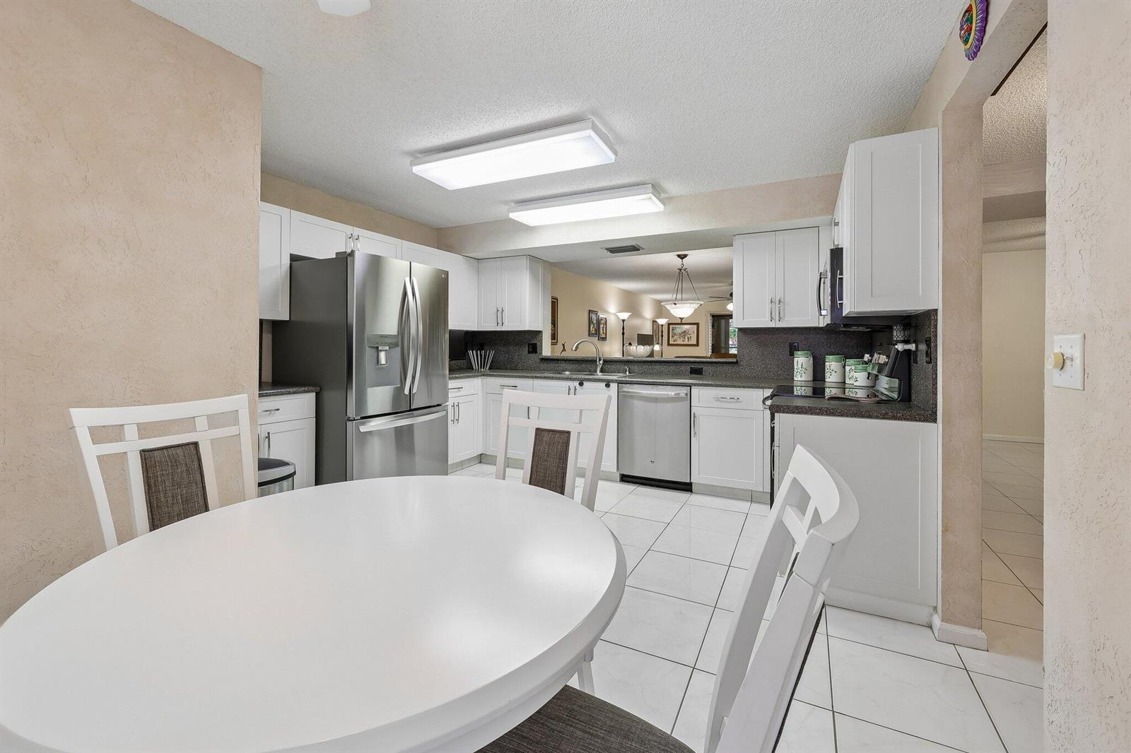 A kitchen features white cabinets, stainless steel appliances, and a dining table in the foreground — 9681 E Sills Dr E # 102, Boynton Beach FL 33437, BOYNTON BEACH, FL