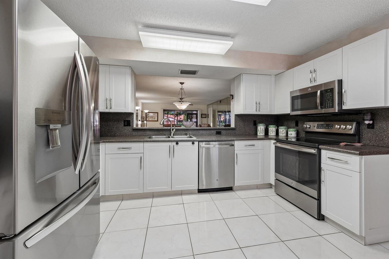 A kitchen with white cabinets, stainless steel appliances, dark countertops, and white tile flooring — 9681 E Sills Dr E # 102, Boynton Beach FL 33437, BOYNTON BEACH, FL
