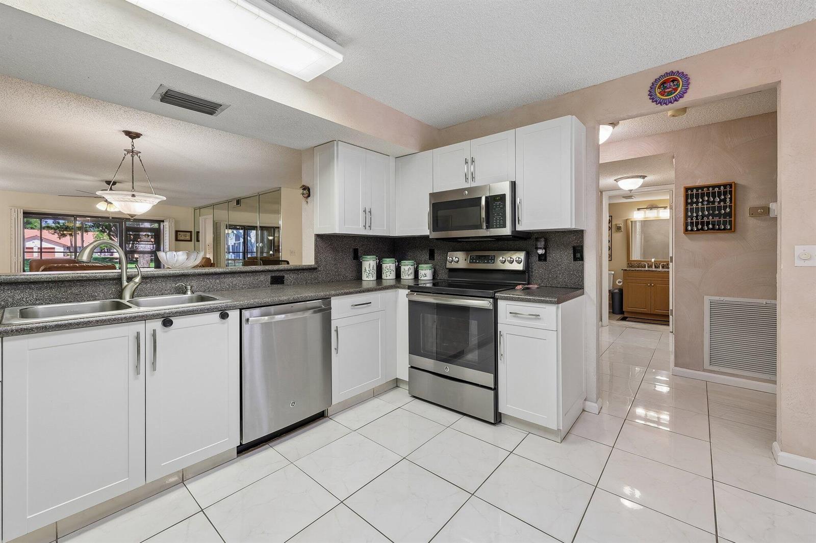 A kitchen with white cabinets, stainless steel appliances, dark countertops, and white tile flooring — 9681 E Sills Dr E # 102, Boynton Beach FL 33437, BOYNTON BEACH, FL