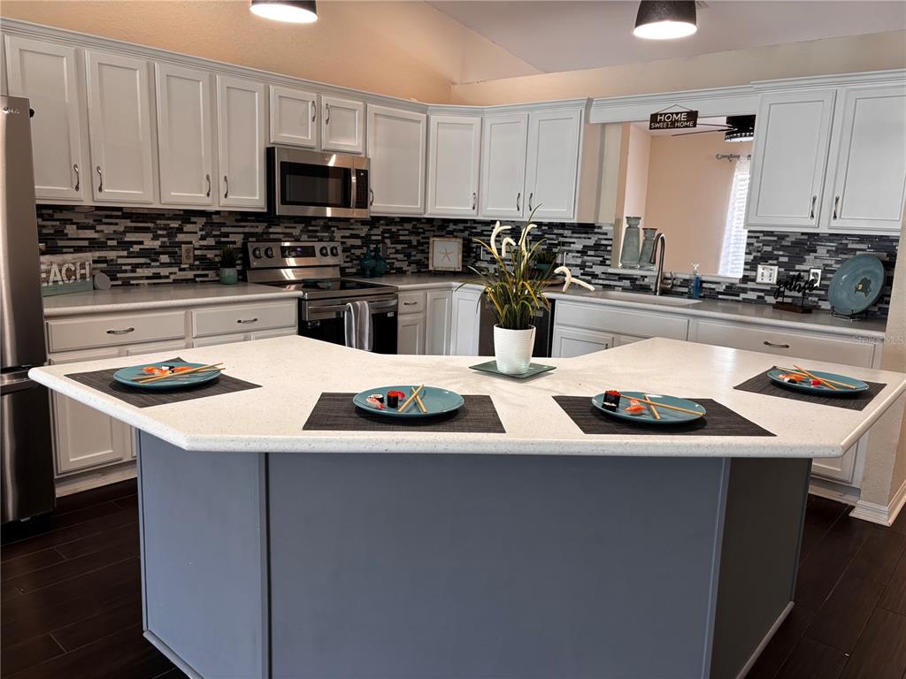 A kitchen features white cabinets, a gray island, a tiled backsplash, and a white countertop — 7855 SUGAR PINE BOULEVARD, LAKELAND, FL