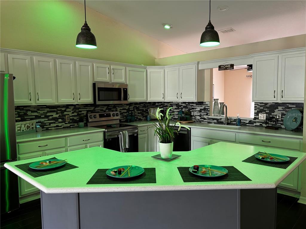 A kitchen features white cabinets, a dark mosaic backsplash, and a large angled island — 7855 SUGAR PINE BOULEVARD, LAKELAND, FL