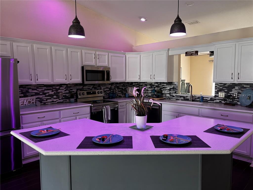 A kitchen features white cabinets, stainless steel appliances, a tiled backsplash, and a large island — 7855 SUGAR PINE BOULEVARD, LAKELAND, FL