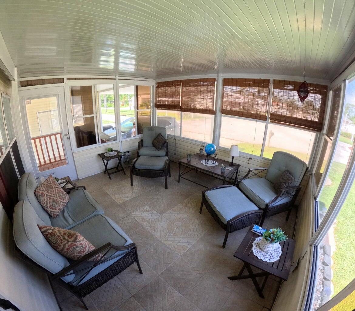 A sunroom with tile flooring, wicker furniture, and large windows overlooking a residential street — 6280 Cypress Lane, Lantana FL 33462, LANTANA, FL
