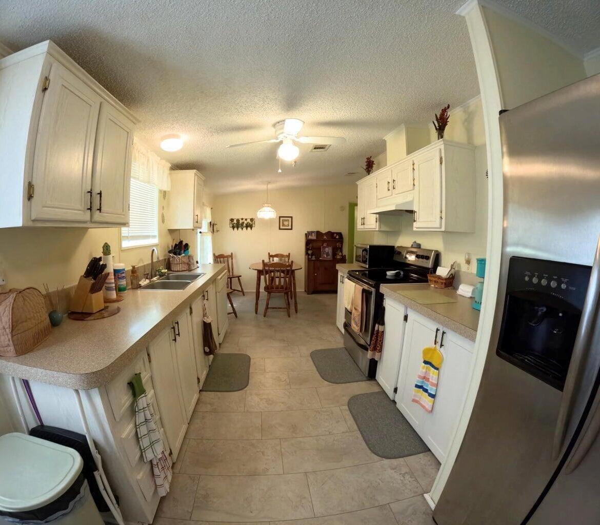 A kitchen with white cabinets, beige countertops, stainless steel appliances, and an adjacent dining area — 6280 Cypress Lane, Lantana FL 33462, LANTANA, FL