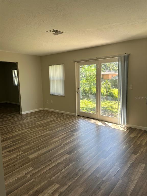 An empty living room features wood-look flooring, a sliding glass door, and a single window — 1795 S LILAC CIRCLE, TITUSVILLE, FL