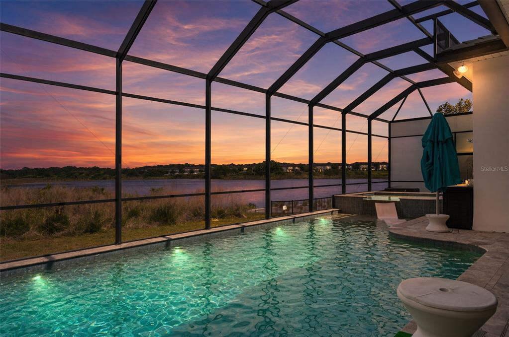 A screened-in pool and spa overlook a lake at sunset — 15522 SHOREBIRD LANE, WINTER GARDEN, FL
