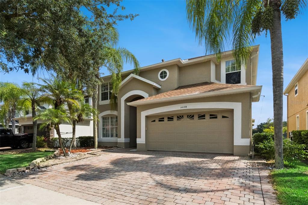 A two-story house with a beige stucco exterior, a brick paver driveway, and palm trees — 14108 BUDWORTH CIRCLE, ORLANDO, FL