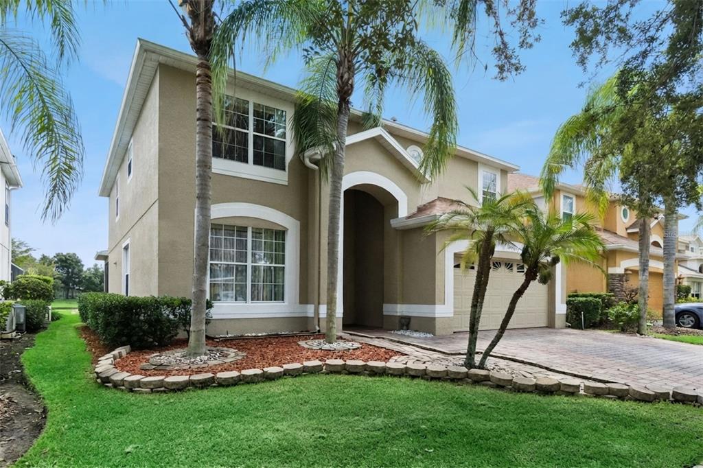 A two-story tan house with a paved driveway, palm trees, and a landscaped front yard — 14108 BUDWORTH CIRCLE, ORLANDO, FL