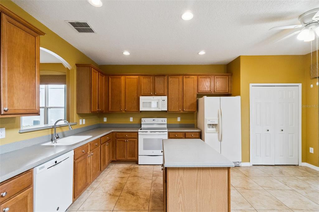A kitchen with wood cabinets, white appliances, a center island, and tan tile flooring — 14108 BUDWORTH CIRCLE, ORLANDO, FL