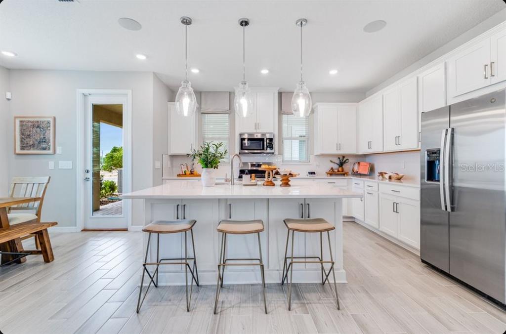 A modern white kitchen features a large center island with three stools and stainless appliances — 5178 GOLDFINCH STREET, ST CLOUD, FL