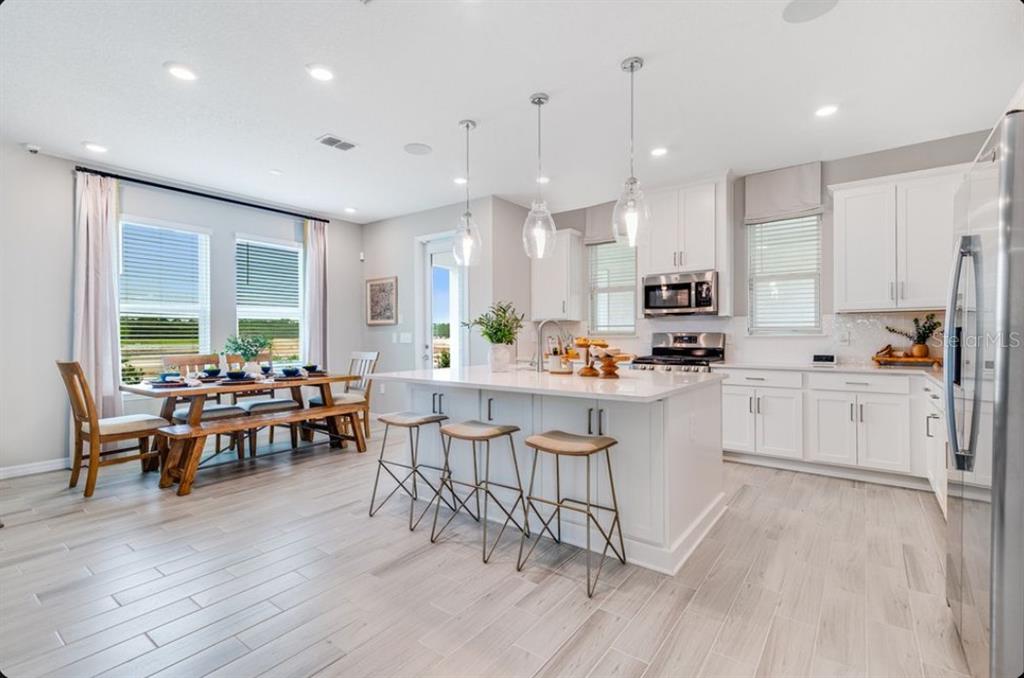 A bright kitchen features white cabinets, a central island with bar stools, and a dining area — 5178 GOLDFINCH STREET, ST CLOUD, FL