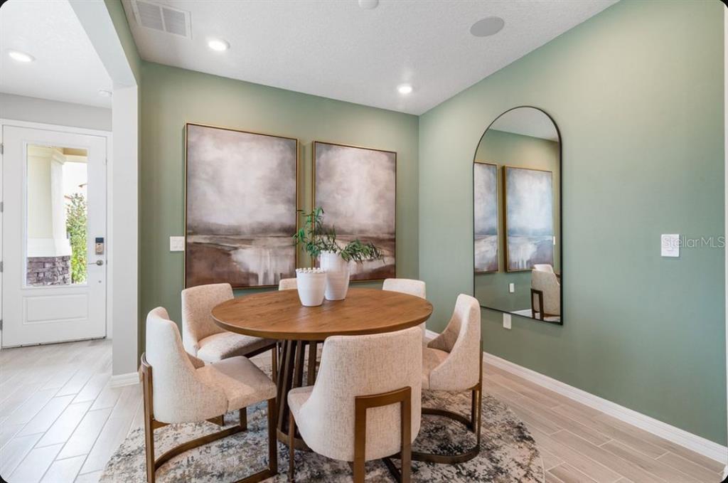 A dining room features a round wooden table, upholstered chairs, sage green walls, and artwork — 5178 GOLDFINCH STREET, ST CLOUD, FL