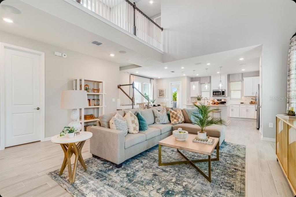 A bright, open-concept living room features a sectional sofa, area rug, and a kitchen beyond — 5178 GOLDFINCH STREET, ST CLOUD, FL