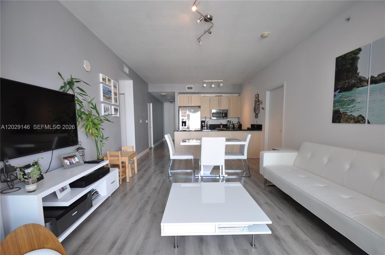A living room and kitchen area feature light wood-look flooring, white furniture, and gray walls — 79 SW 12th St, Miami FL 33130, MIAMI, FL